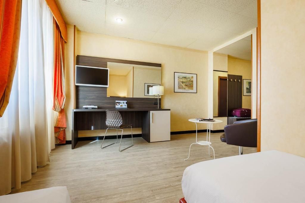 Una habitación de hotel con cama, escritorio, silla, mesita, espejo y armario.