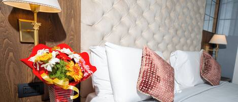 A hotel room with a tufted headboard, a bedside lamp, a vase with flowers, and a bed with white bedding and patterned pillows.