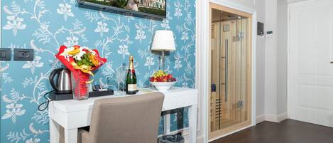 Habitación de hotel con una mesa blanca, un ramo de flores, una botella de champán y un cuenco de fruta.