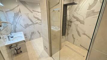 A modern bathroom with a glass-enclosed shower, a sink with a handheld showerhead, and marble-patterned walls.