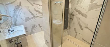 A modern bathroom with a glass-enclosed shower, a sink with a handheld showerhead, and marble-patterned walls.