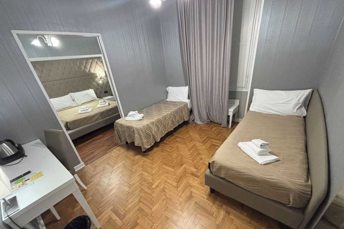 Ein Hotelzimmer mit zwei Betten, einem Schreibtisch, einem Spiegel und Holzboden.
