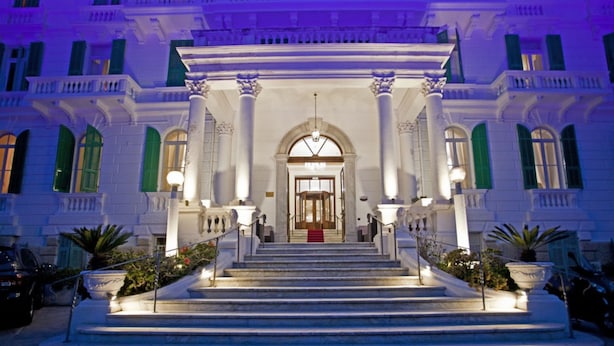 A grand entrance with a central staircase leading to a door, flanked by columns and potted plants. - Grand Hotel & des Anglais (Sanremo)