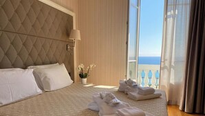 A hotel room with a large bed, a nightstand, a lamp, a potted plant, and a view of the sea through the balcony. - Grand Hotel & des Anglais (Sanremo)