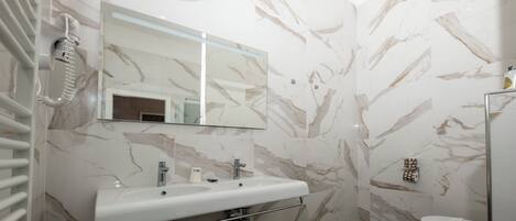 Ein Badezimmer mit Marmorwand, Waschbecken mit Spiegel, Toilette und Duschbereich.