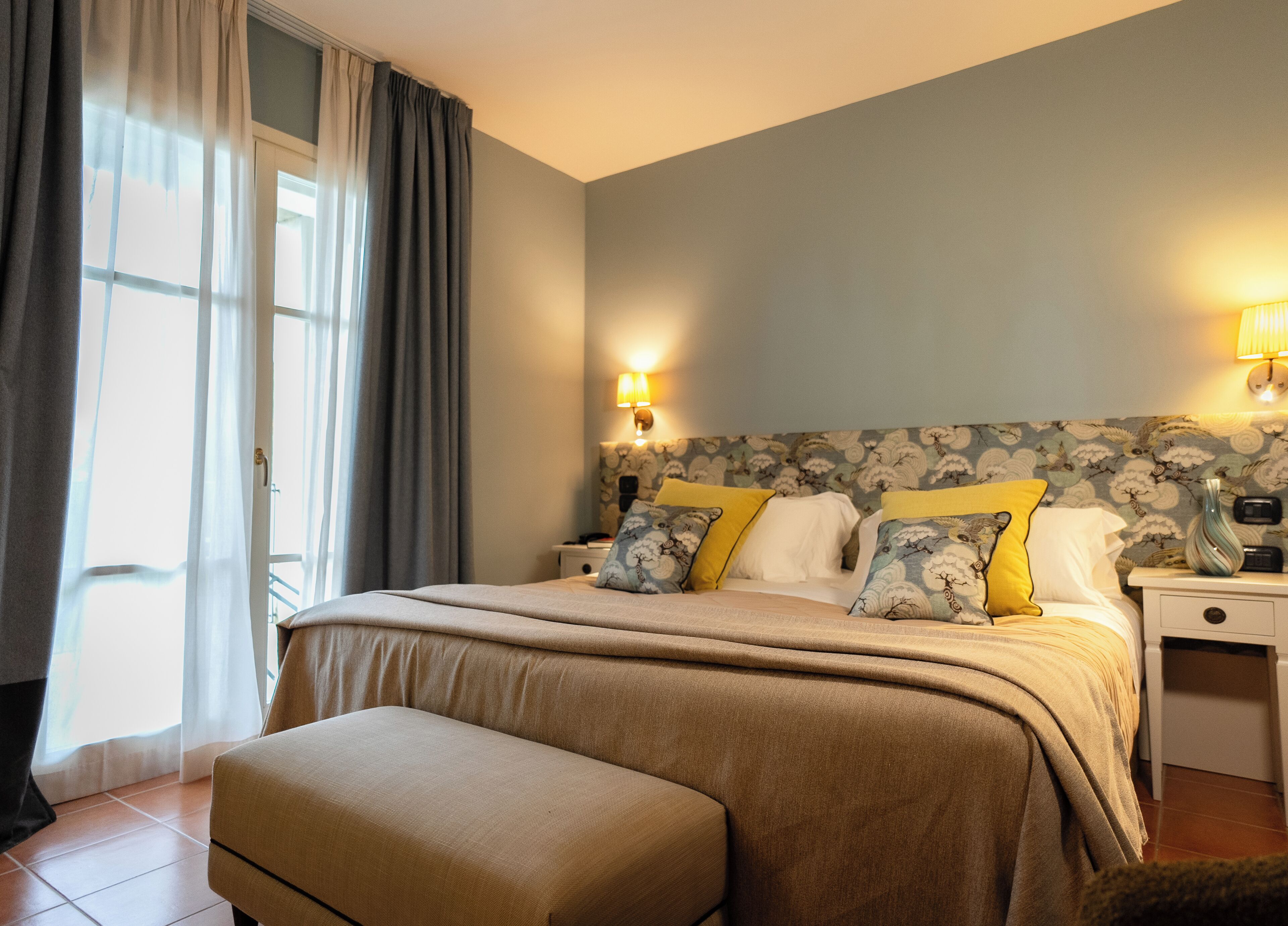 A bedroom with a bed, bedside tables, a nightstand, a lamp, and a window with curtains.