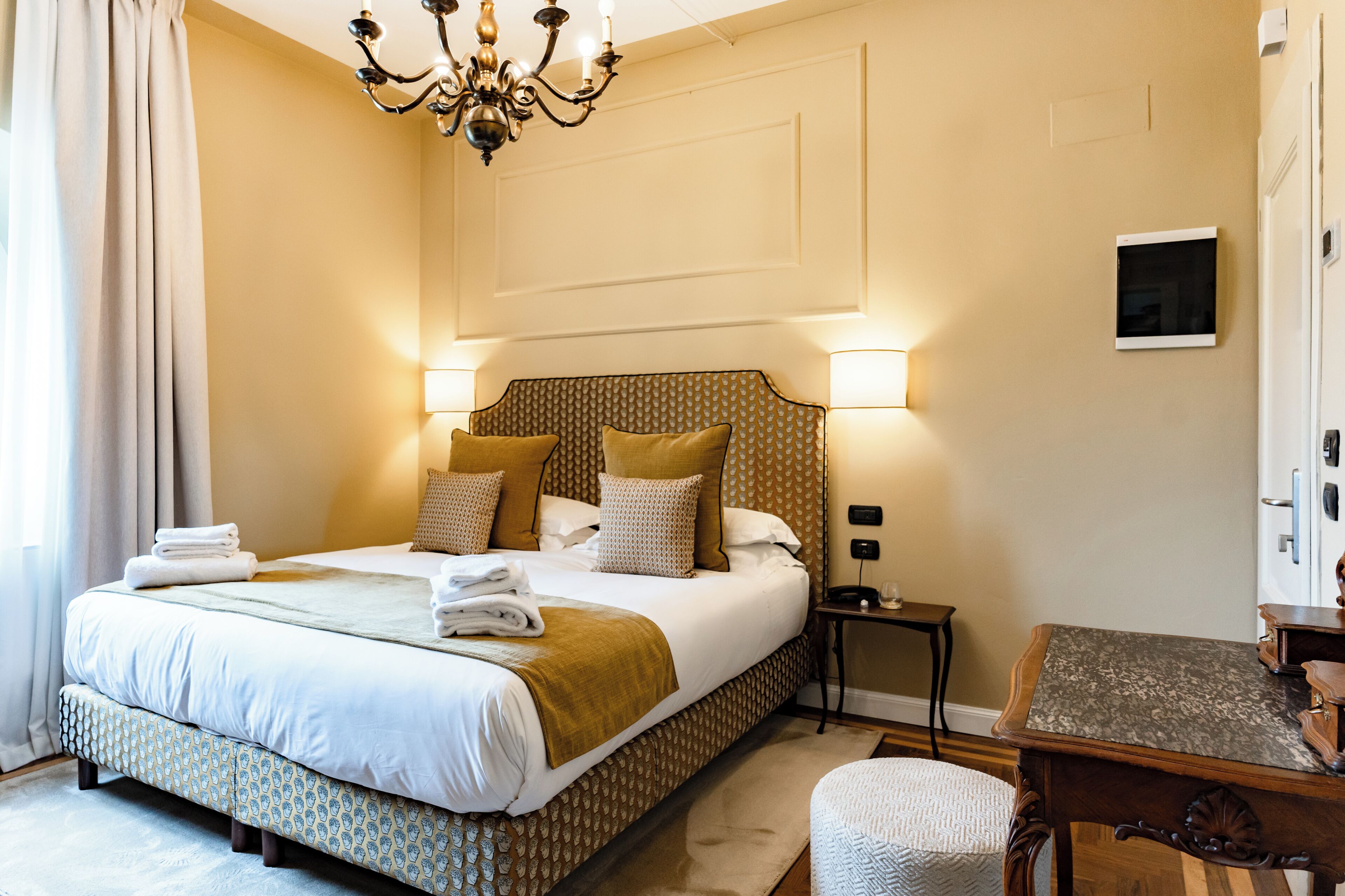 A hotel room with a large bed, bedside lamps, a small table, and a chair.