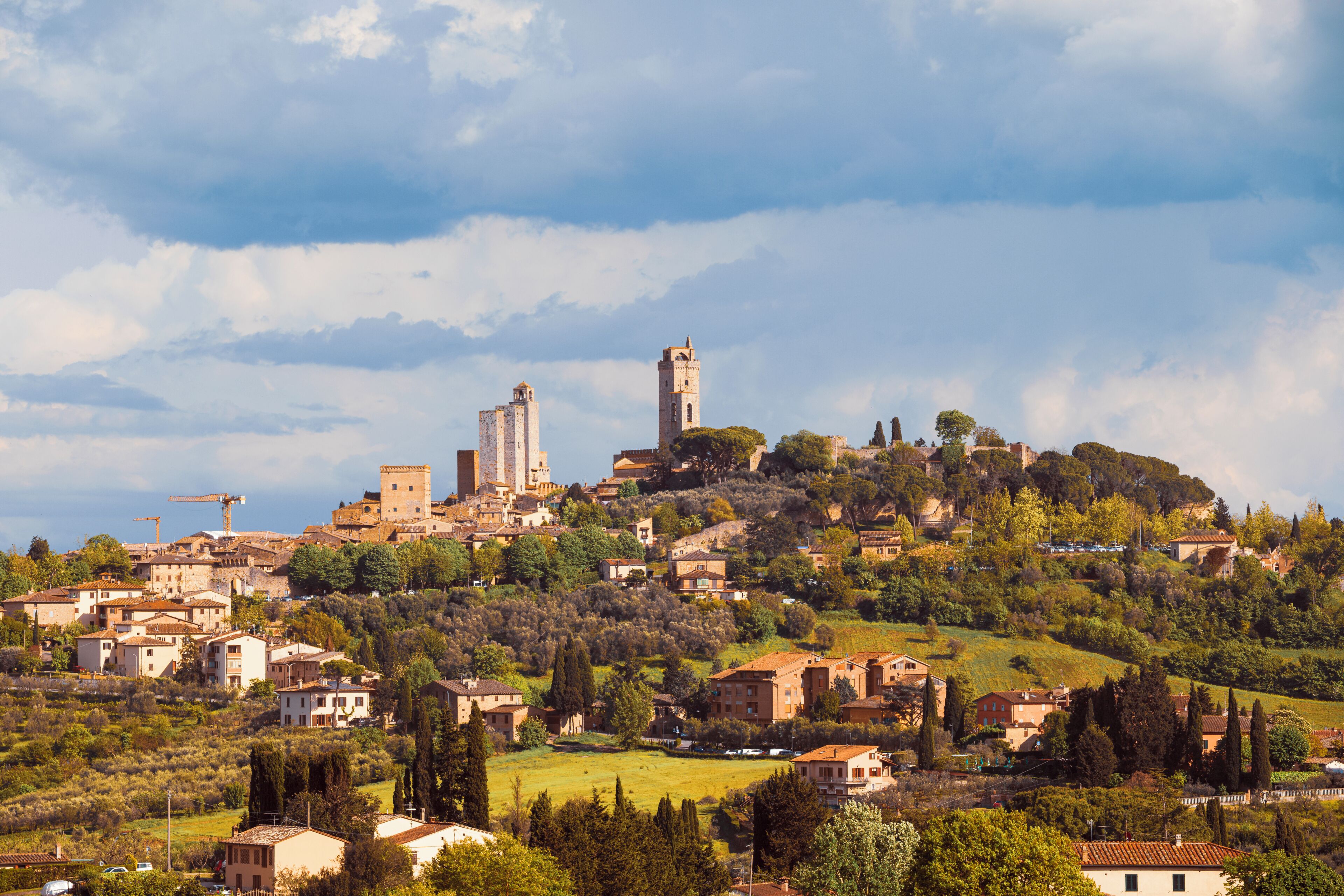 A historic town with a prominent tower and castle on a hill, surrounded by greenery and traditional buildings.