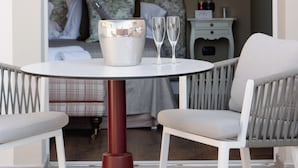 A hotel room with a bed, a bedside table with a lamp, a small table with two glasses, and a chair. - Cappuccina Country Resort (San Gimignano)