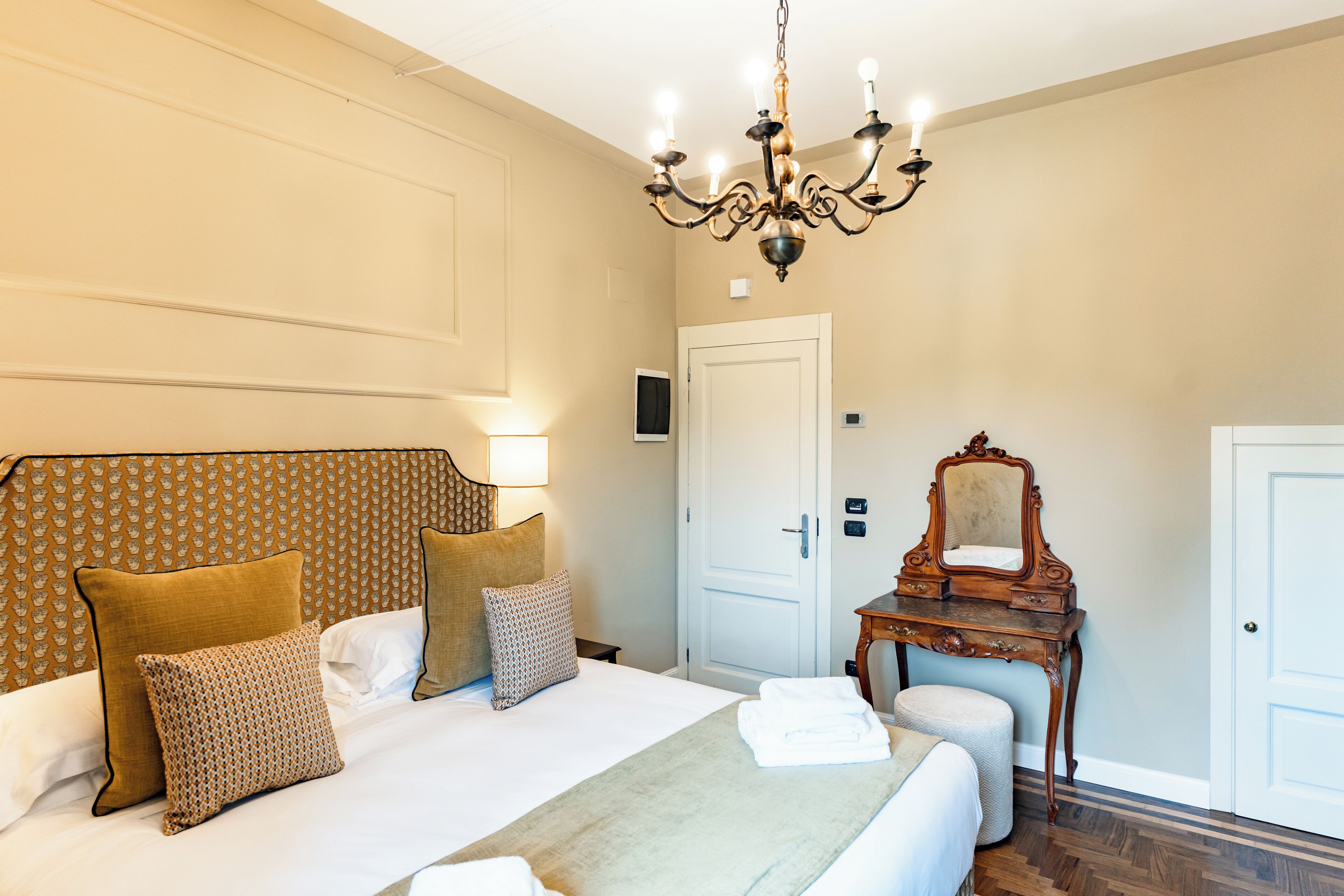 Una habitación de hotel con una cama grande, una araña, un aparador de madera y una puerta.