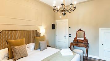 Una habitación de hotel con una cama grande, una araña, un aparador de madera y una puerta.