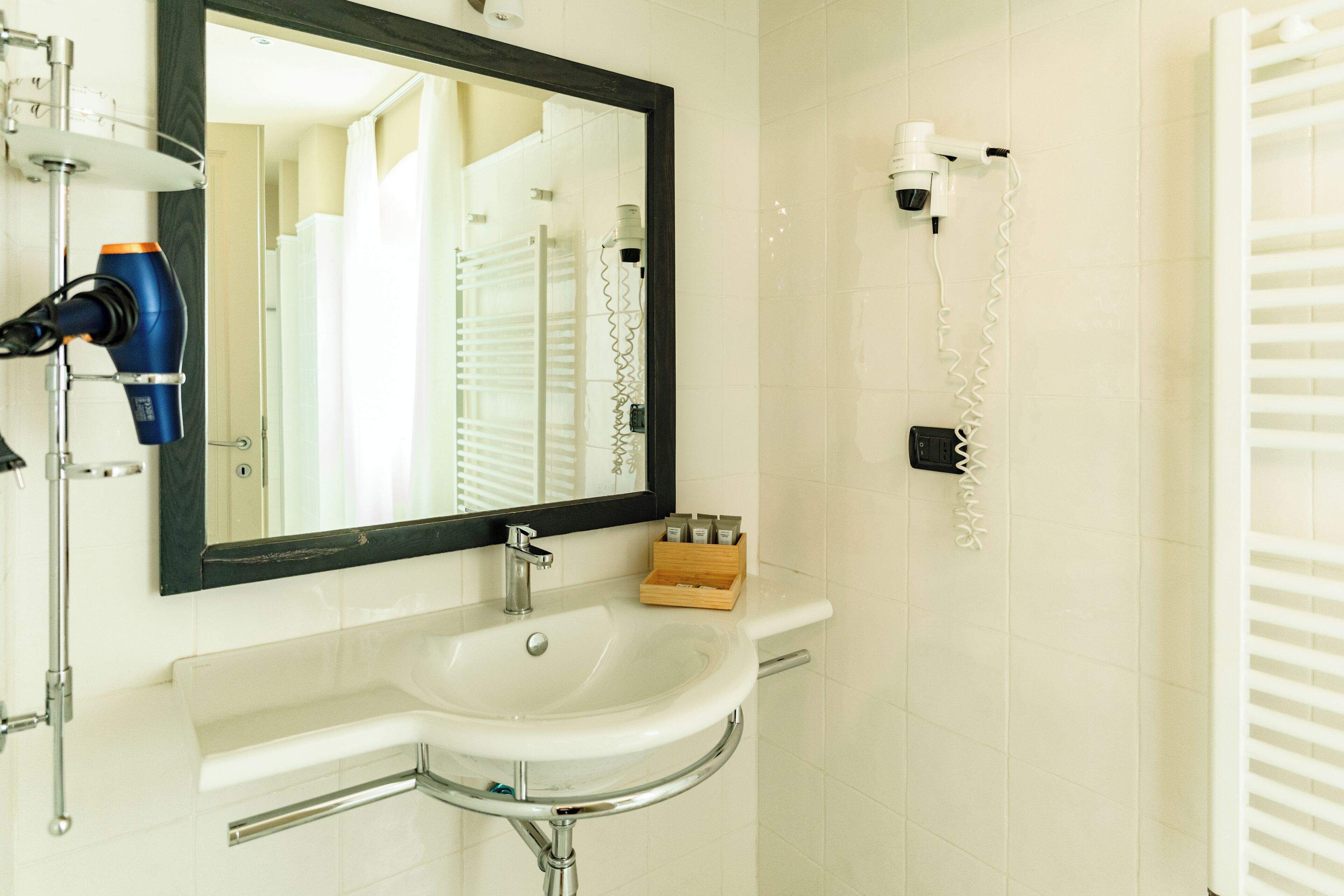 Een badkamer met een wit wastafelmeubel, een spiegel, een haardroger en een handdoekhouder.
