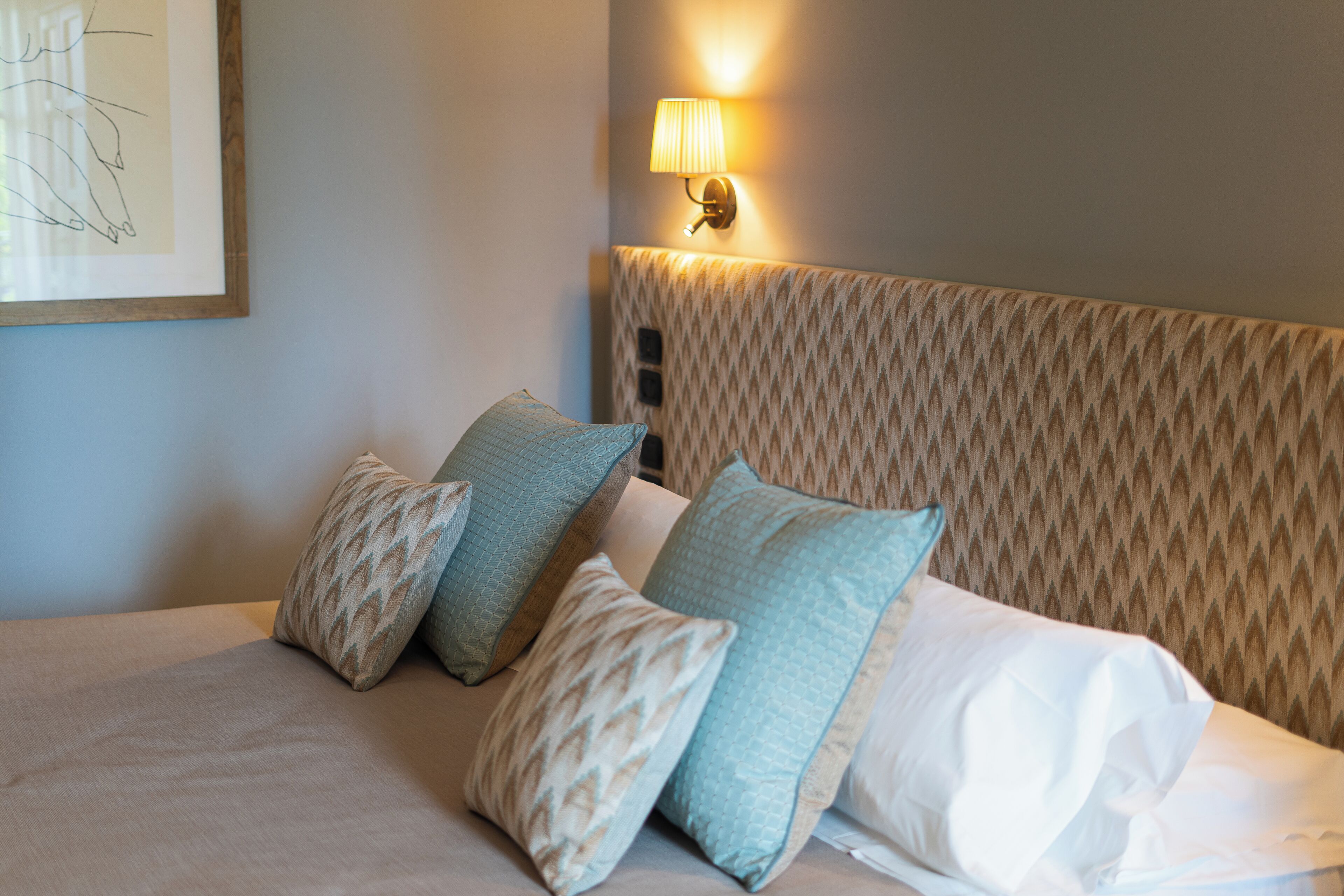 Un letto con cuscini decorati e una testiera dal disegno materico.