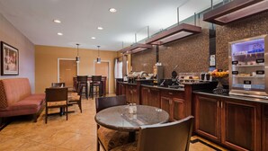 A hotel dining area with a bar, seating, and a kitchen in the background.