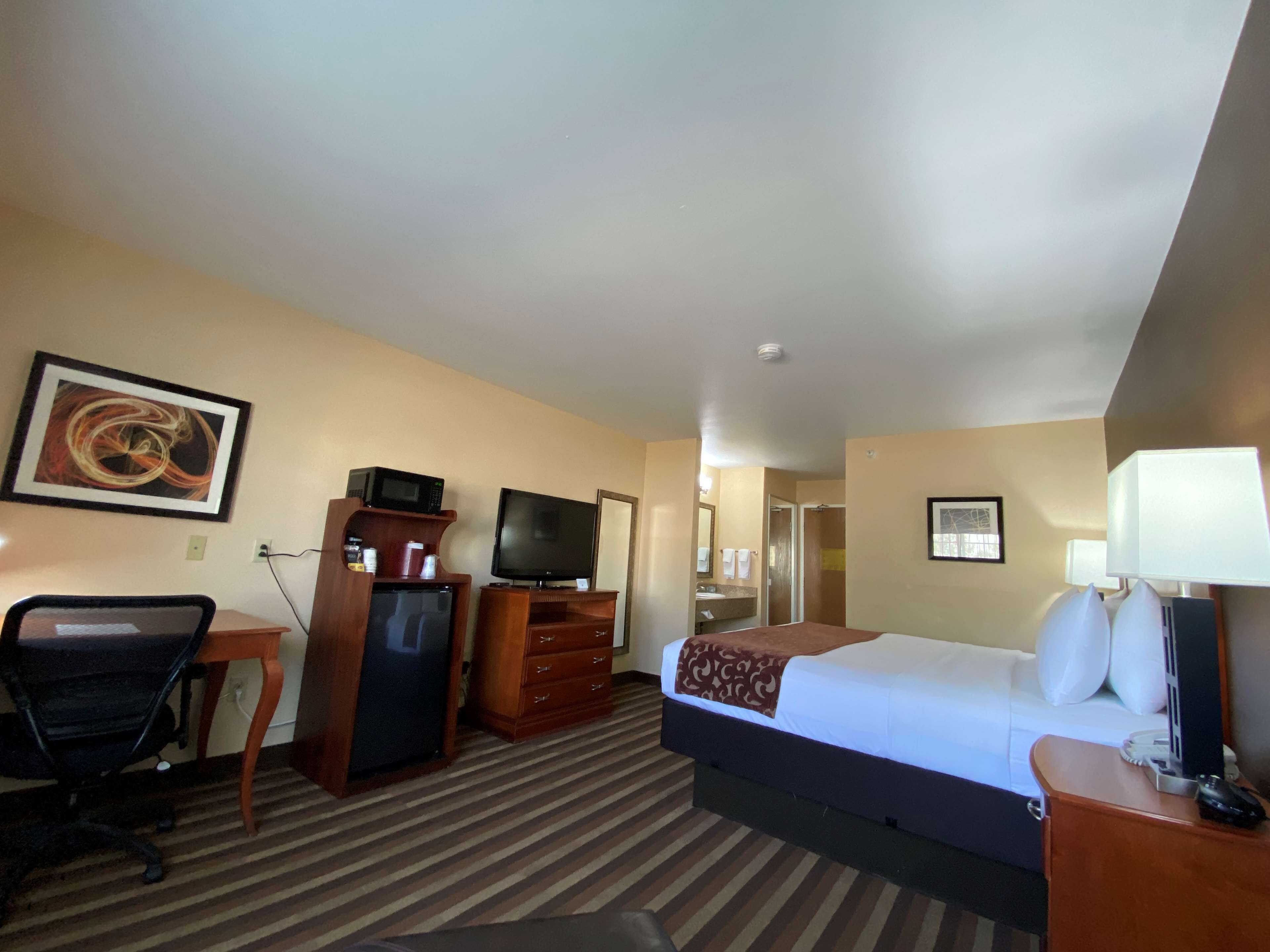 A hotel room with a bed, a desk, a television, a dresser, and a bathroom visible through an open door.