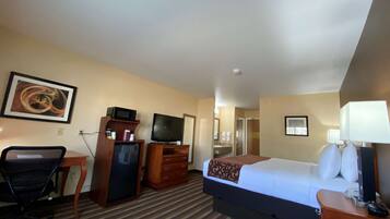 A hotel room with a bed, a desk, a television, a dresser, and a bathroom visible through an open door.