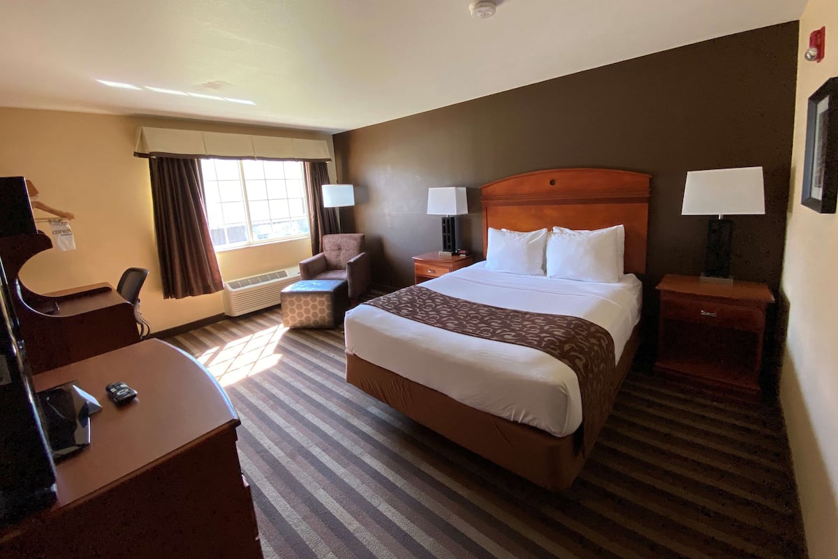 A hotel room with a large bed, two bedside tables with lamps, a desk with a chair, a window with curtains, and a radiator.