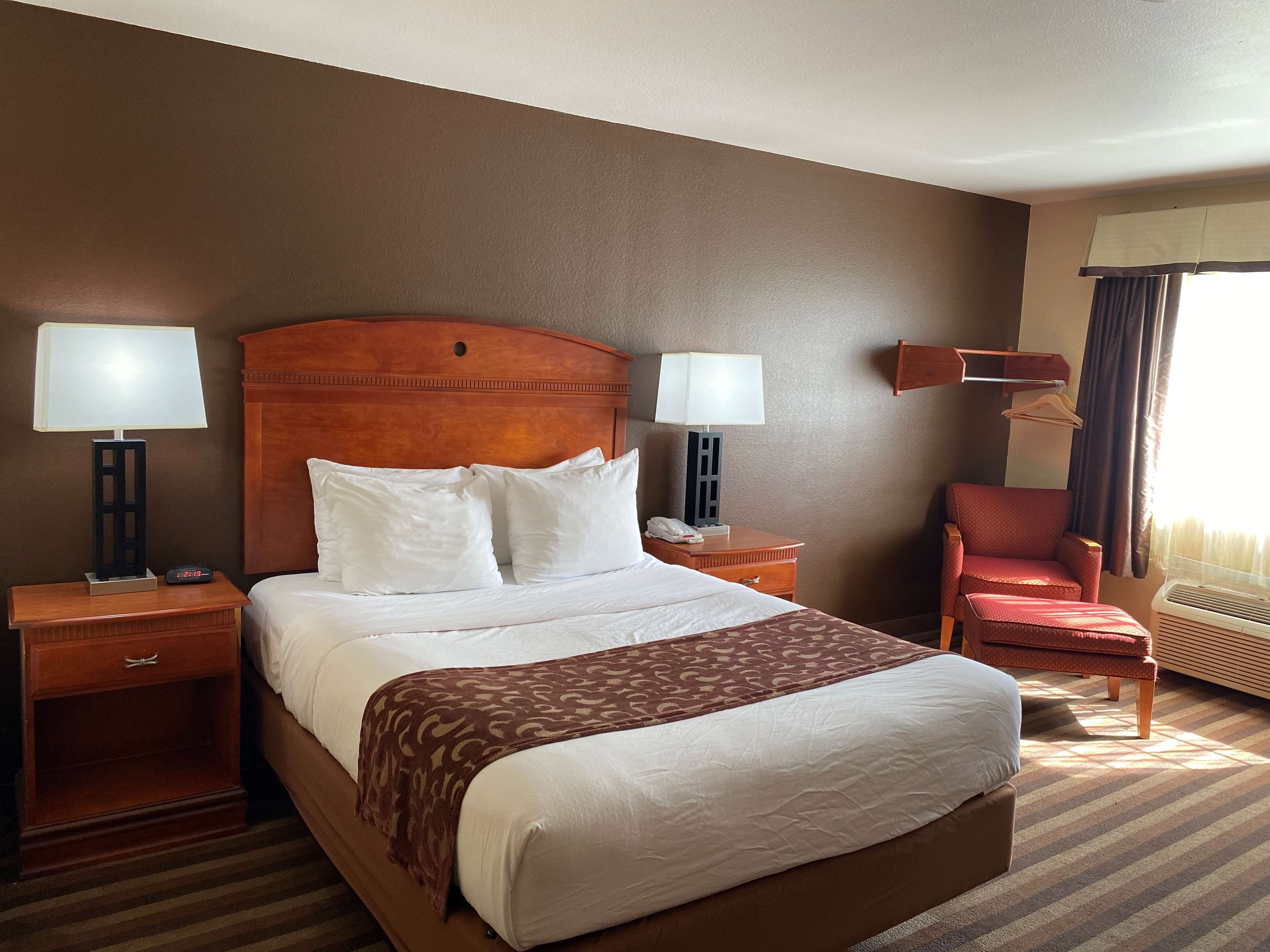 A hotel room with a large bed, two bedside tables, a chair, a desk, and a window with curtains.