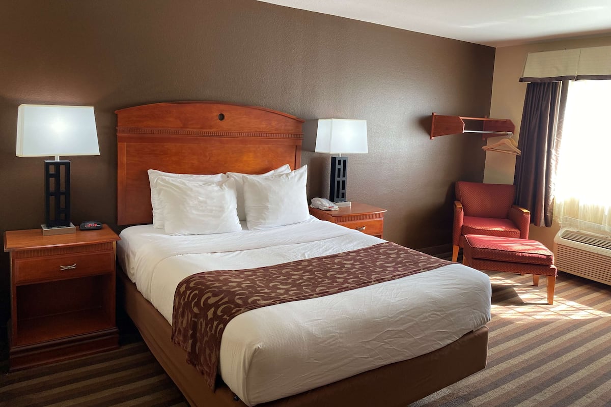 A hotel room with a large bed, two bedside tables, a chair, a desk, and a window with curtains.