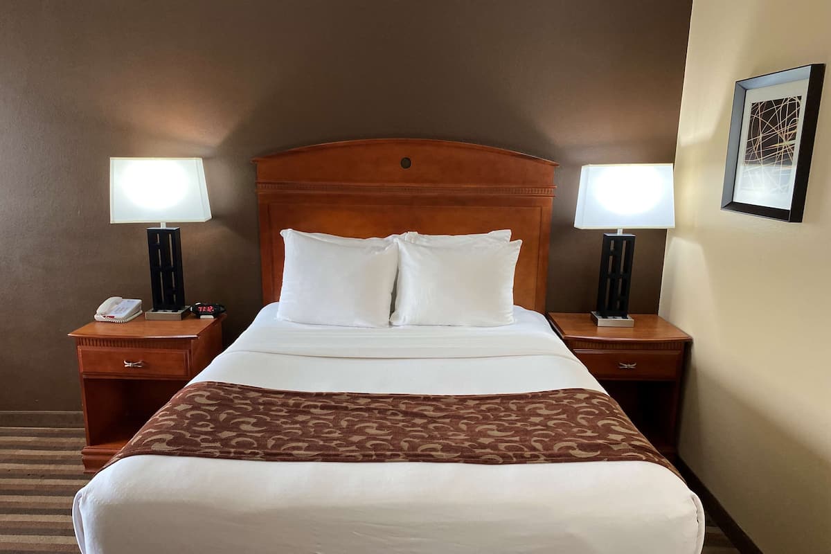 A hotel room with a wooden headboard, two bedside tables with lamps, a telephone, and a framed picture on the wall.