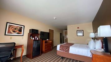 A hotel room with a bed, desk, TV, and a framed artwork on the wall.