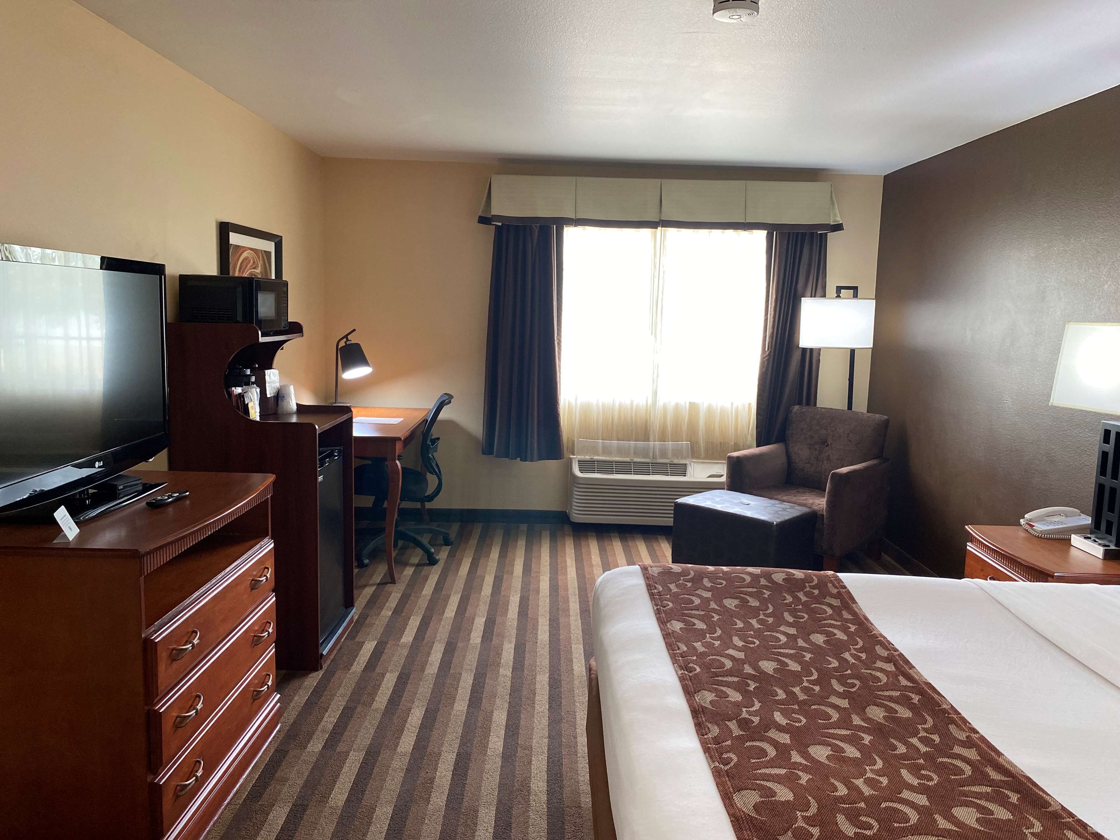 A hotel room with a bed, a desk with a chair, a television, a lamp, and an air conditioning unit.
