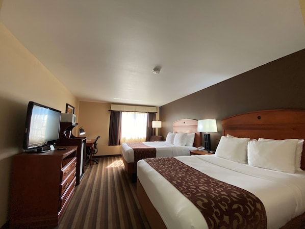 A hotel room with two beds, a desk, a television, and a dresser.
