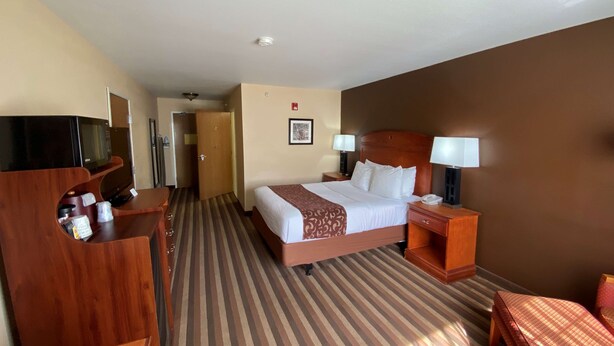 A hotel room with a bed, bedside tables, a desk with a flat-screen TV, a coat rack, and a door leading to a hallway.