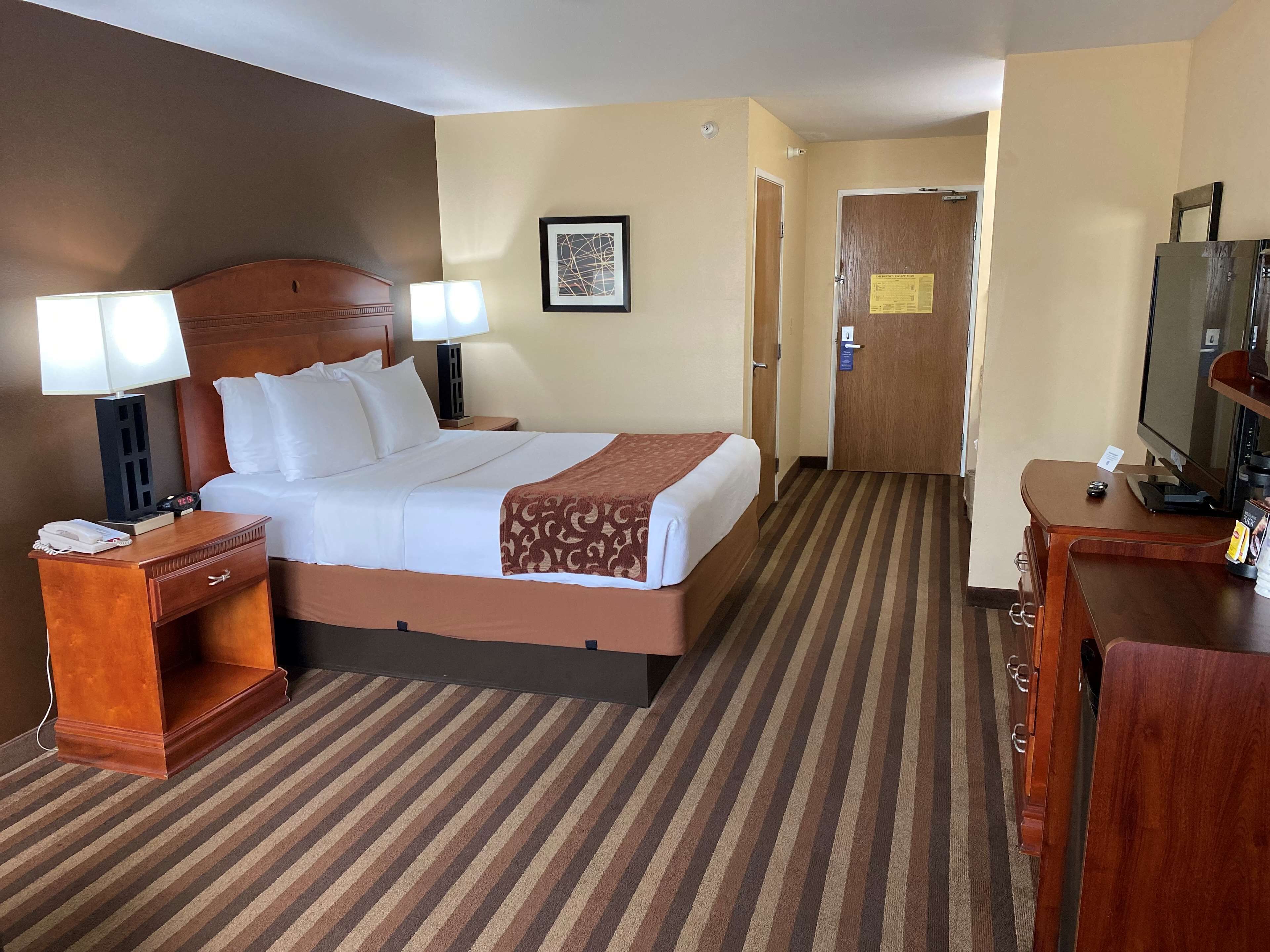 Une chambre d’hôtel comprenant un lit, des lampes de chevet, un bureau avec un téléphone, une télévision et une porte.