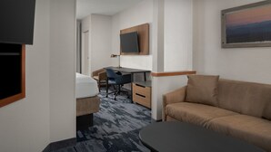 Habitación de hotel con cama, escritorio, silla, sofá, televisión y un cuadro en la pared.