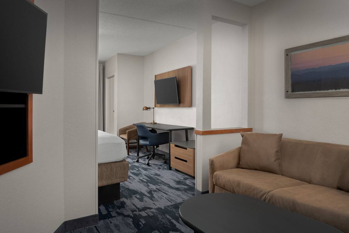 Habitación de hotel con cama, escritorio, silla, sofá, televisión y un cuadro en la pared.