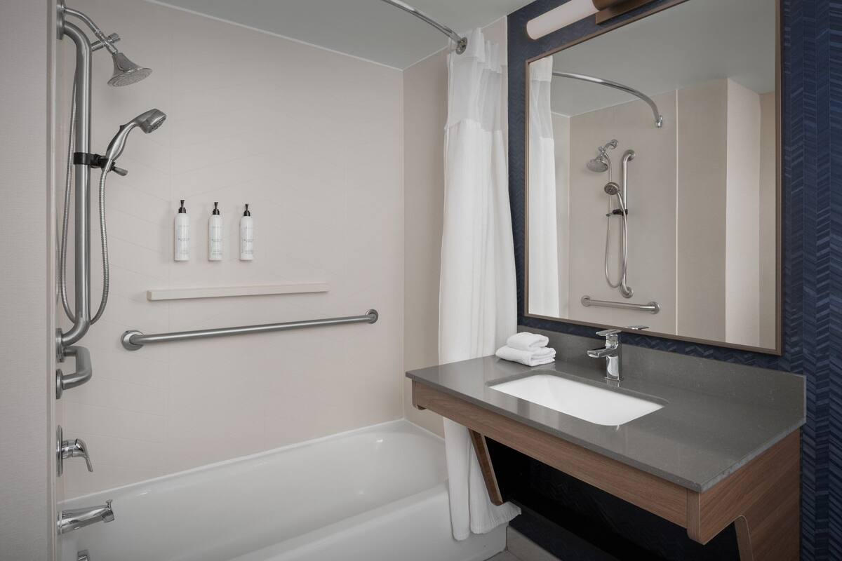 Un baño moderno con bañera, tocador con lavamanos, espejo y ducha con cabezal de ducha de mano.