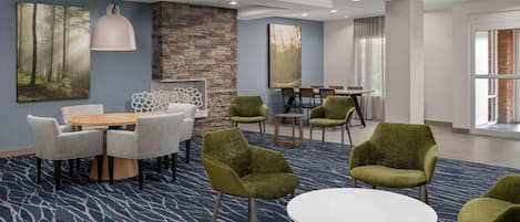 Um lobby de hotel moderno com uma mesa redonda, cadeiras verdes, uma parede de destaque em pedra e obras de arte nas paredes.