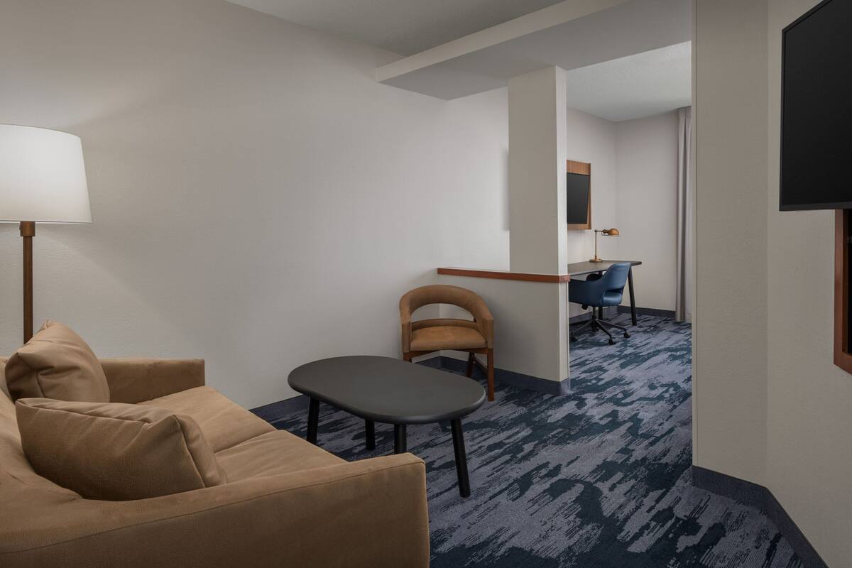 Habitación de hotel con sofá, una mesa pequeña, una silla, un escritorio y un televisor.