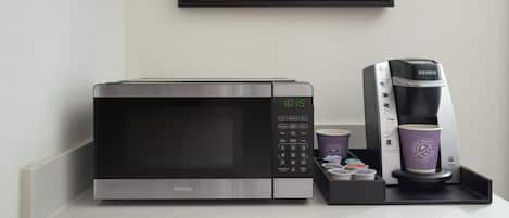 A microwave and coffee maker on a countertop with a framed floral picture above.