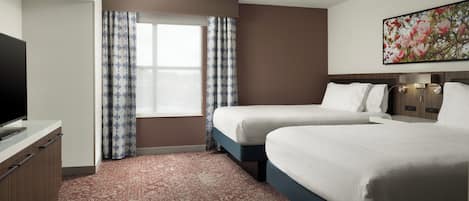A hotel room with two beds, a flat-screen TV, a large window with patterned curtains, and a floral artwork on the wall.