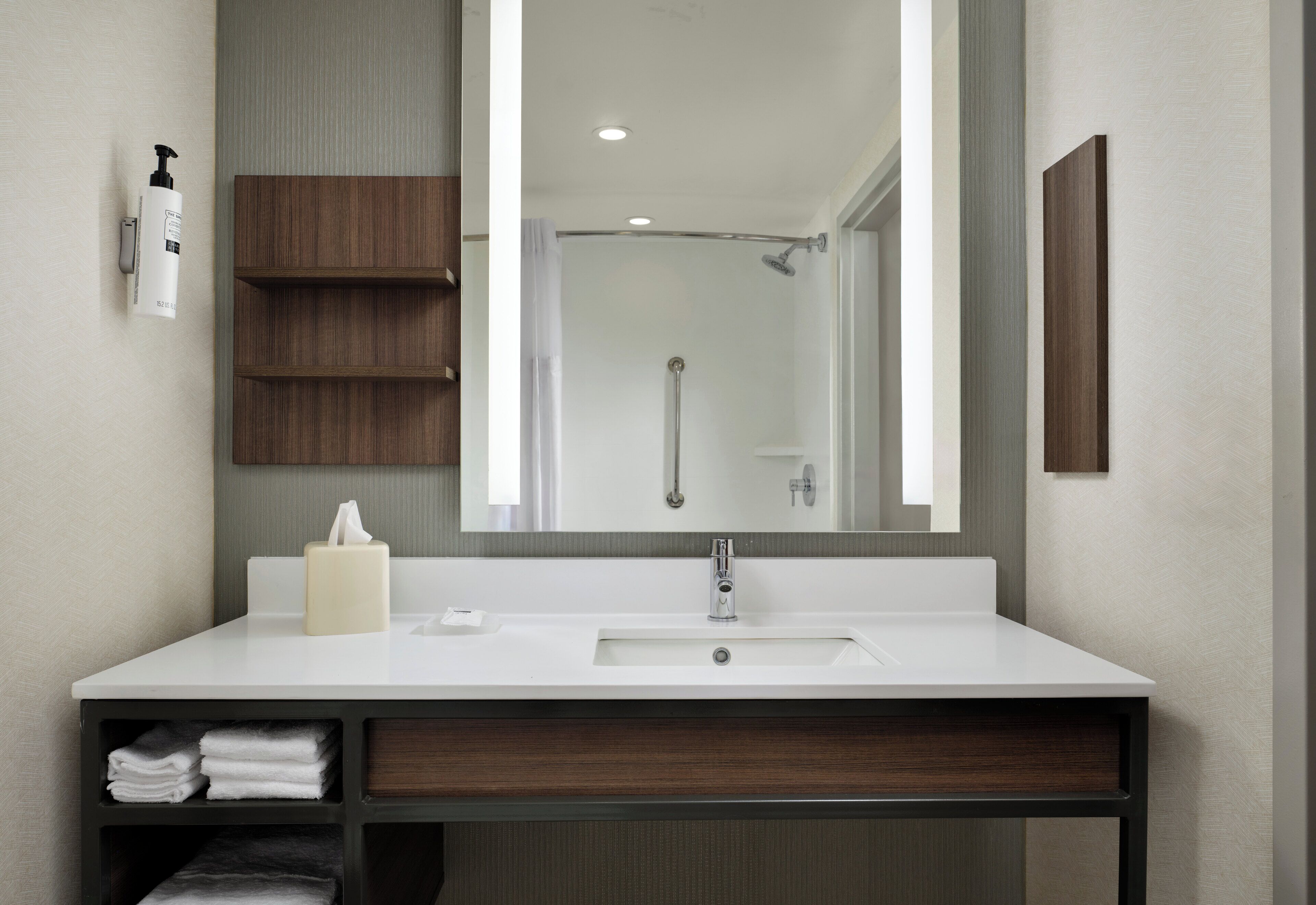 Un baño moderno con lavamanos blanco, un espejo grande, un armario de madera y una zona de ducha.