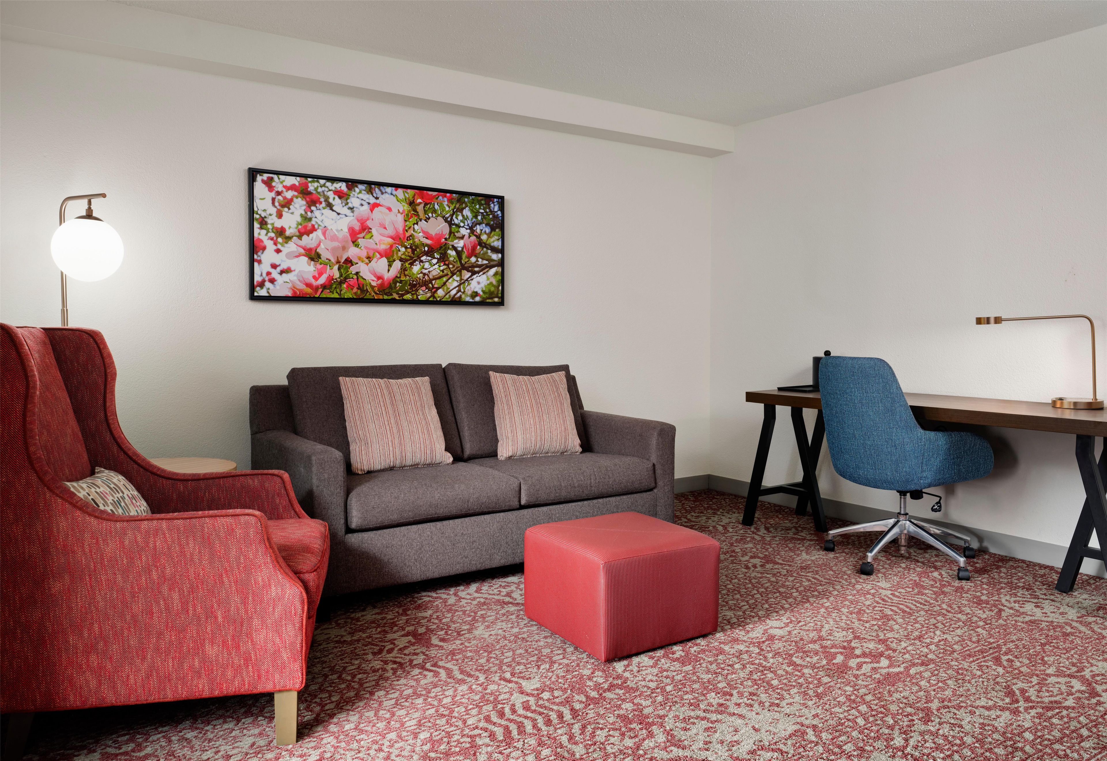 Una sala de estar con un sofá, un sillón rojo, un escritorio y una silla.
