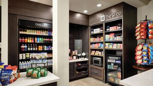 A hotel room with a kitchenette area, including a fridge labeled 'CHILLED' and 'FROZEN', a microwave, and a coffee maker. There is a small shop area with snacks and beverages. - Hilton Garden Inn Jackson/Madison (Madison)