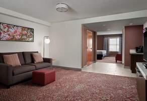 Una habitación de hotel moderna con sofá, reposapiés y un cuadro floral grande en la pared.