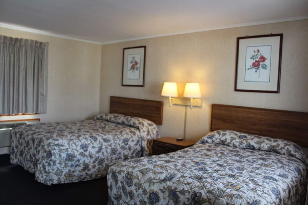 A hotel room with two beds, a nightstand, a lamp, and framed floral artwork on the walls.