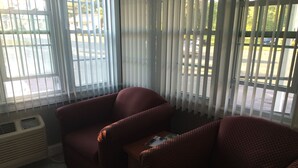 Quarto com duas poltronas vermelhas, uma mesa pequena e uma janela com persianas.