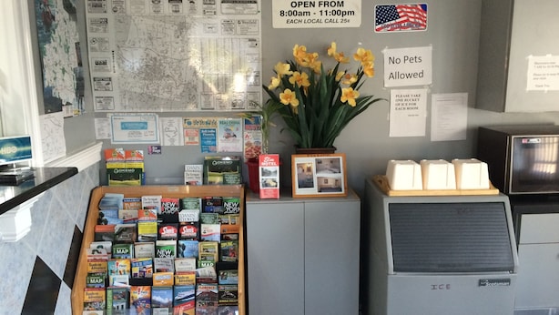 Uma área de recepção de hotel com um mapa, um relógio, uma placa indicando o horário de check-out, uma placa proibindo animais de estimação e uma estante com livros de viagem.