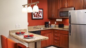 Una cocina con encimeras de granito, armarios de madera, refrigerador de acero inoxidable, microondas, cafetera y comedor con mesa y sillas.