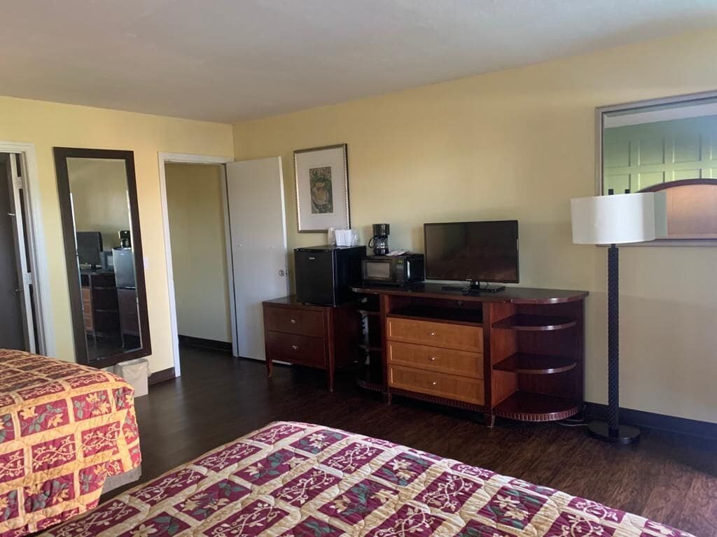 Habitación de hotel con cama, escritorio con televisor, cafetera y lámpara.