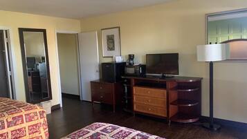 Habitación de hotel con cama, escritorio con televisor, cafetera y lámpara.