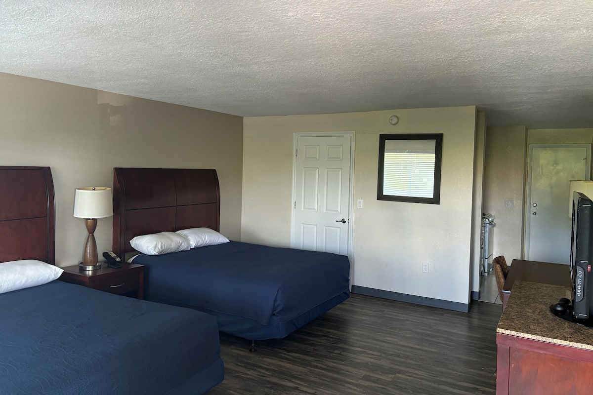 A hotel room with two beds, a desk, a lamp, and a television.