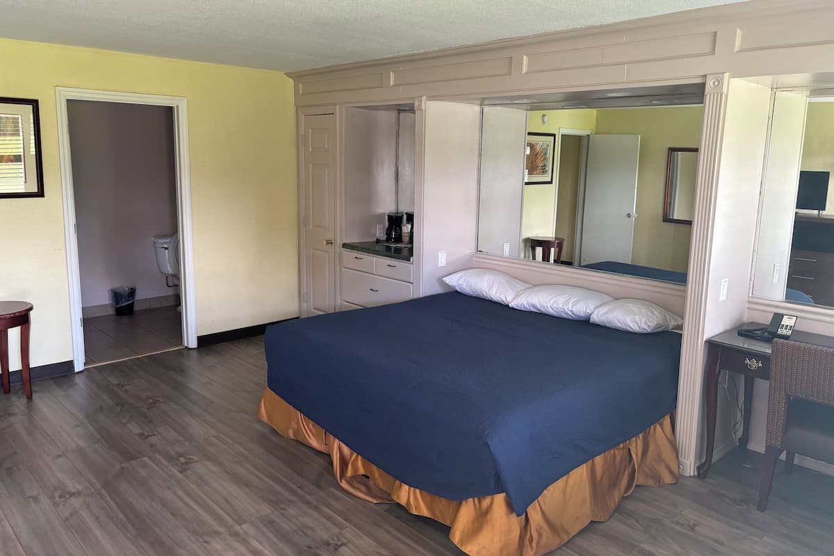 A bedroom with a bed, a dresser, a mirror, and a door leading to a bathroom.