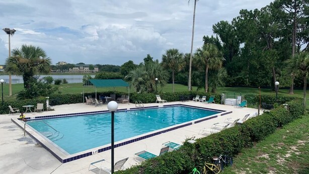 Une piscine rectangulaire dont le bord est recouvert de carrelage, entourée de chaises longues et d’un vélo.