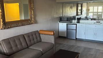 A living room with a sofa, a coffee table, and a kitchen area with cabinets and appliances.